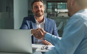 Business professionals shaking hands across a desk during a meeting with a laptop