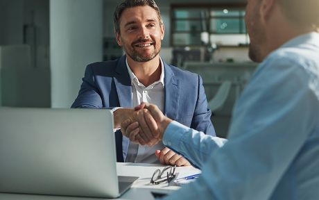 Business professionals shaking hands across a desk during a meeting with a laptop