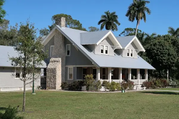 Gray two-story home with front porch, stone chimney, and palm trees