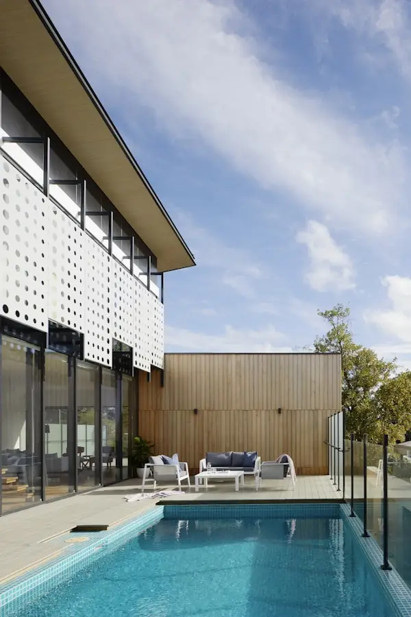 Modern home patio with swimming pool, outdoor seating, and glass walls