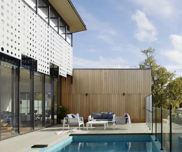 Modern home patio with swimming pool, outdoor seating, and glass walls