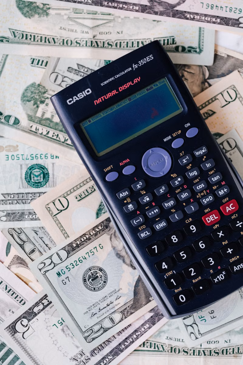 Scientific calculator resting on scattered U.S. dollar bills
