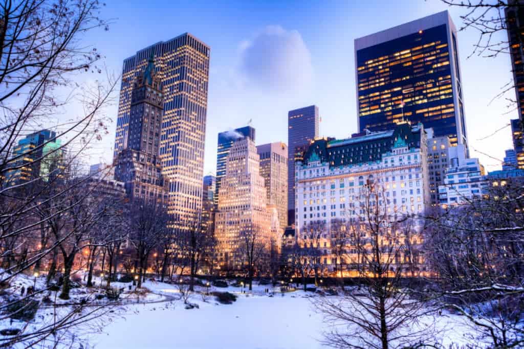 Snow-covered urban park surrounded by illuminated high-rise buildings at dusk