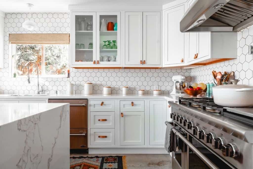 Bright remodelled kitchen with white cabinets, marble island, tile backsplash, and stainless-steel appliances