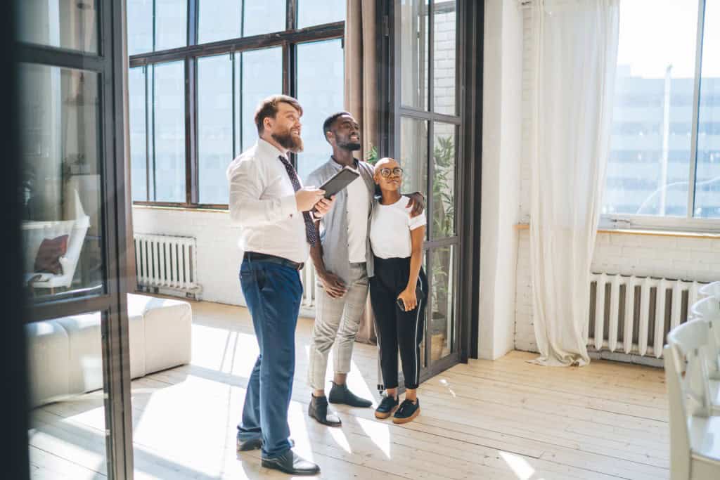 Real estate professional showing a bright apartment to a smiling couple during a property tour