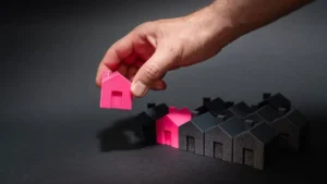 Hand selecting a pink house model from a row of dark homes