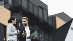 Two real estate professionals discussing documents outside a modern building