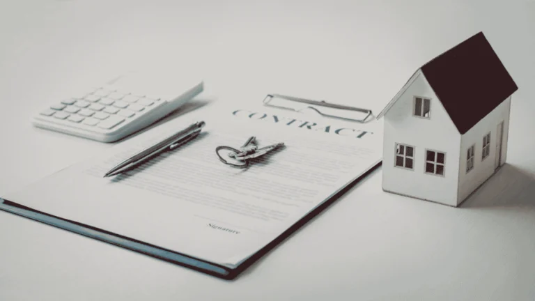 Home model beside real estate contract, keys, calculator, and pen