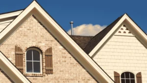 Brick and siding home rooflines with arched windows under blue sky