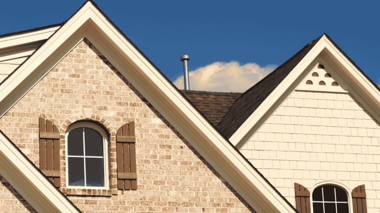 Brick and siding home rooflines with arched windows under blue sky