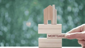 Hand placing a mortgage block beneath a wooden house model