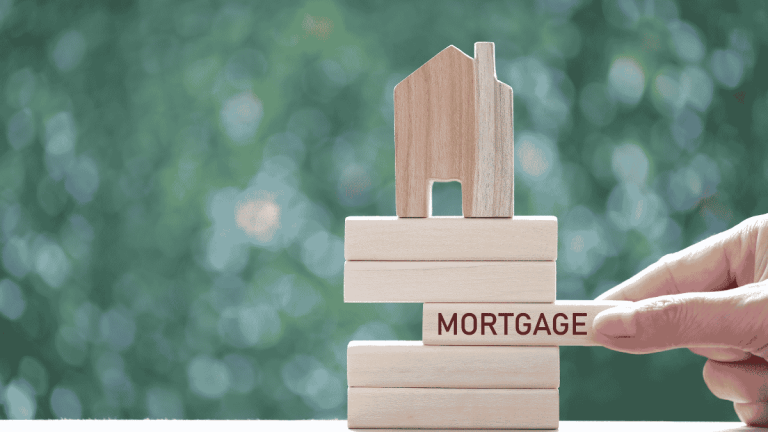 Hand placing a mortgage block beneath a wooden house model