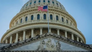 U.S. Capitol dome with American flag against a clear blue sky